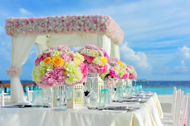 prostřený svatební stůl někde na pláži, výrazné květiny na stole, prostřeno na bílo