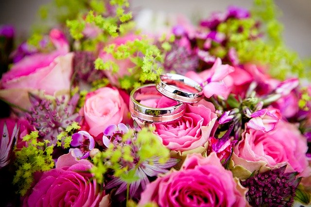 kytice z růžových květin a na ní jsou položené dva snubní prsteny